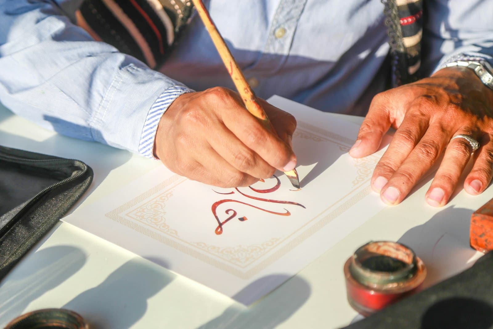 A calligrapher writing Arabic letters with a qalam